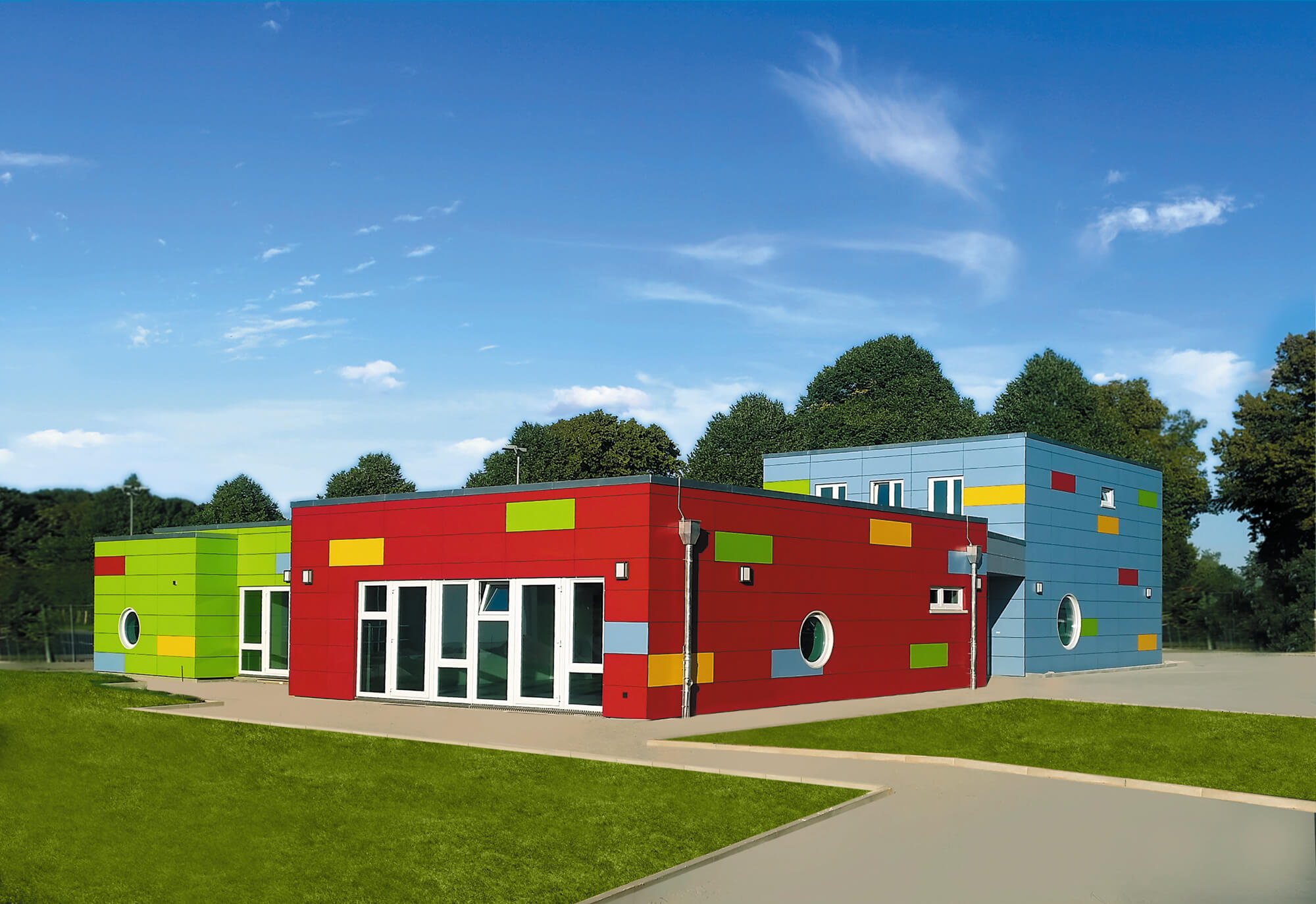 Moderne Kindertagesstätte aus drei farbigen Gebäudeteilen in Rot, Grün und Blau mit bunten Fensterelementen.