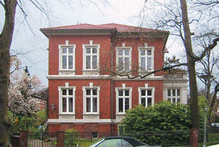 Aufwendig sanierte Altbauvilla mit markanter roter Fassade, weiß umrandeten Fenstern und historischer Architektur.