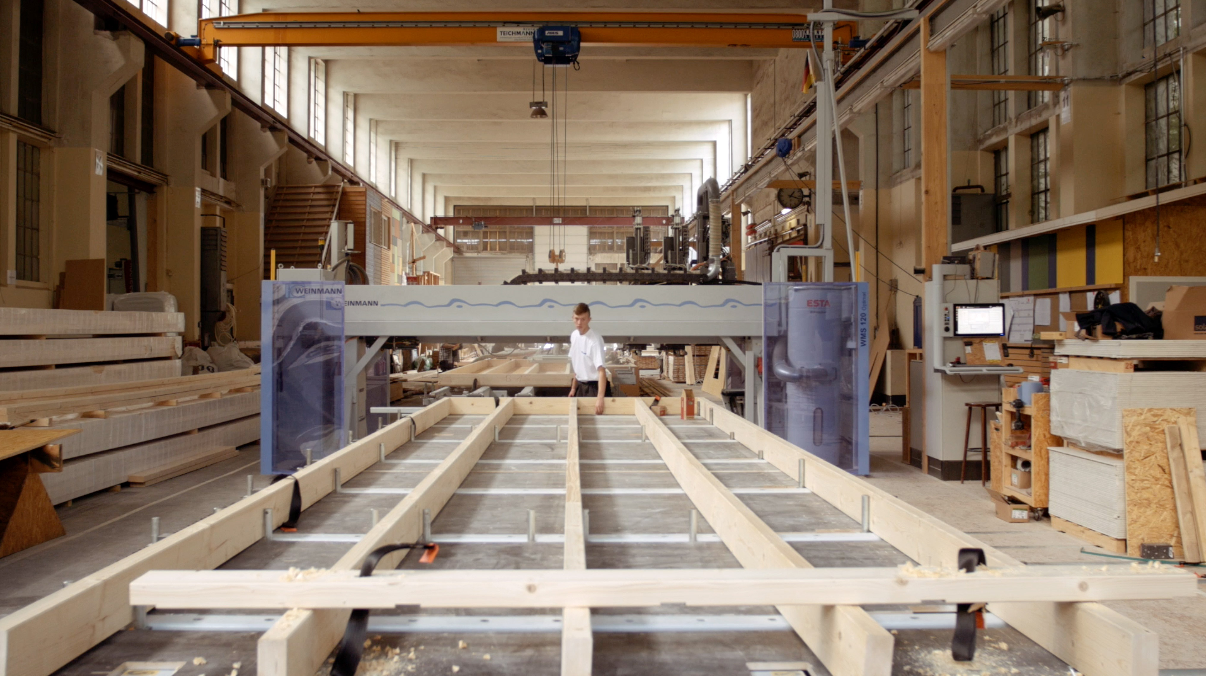 Zimmerer steht an einer automatisierten Holzbau-Fertigungsmaschine, die Wandelemente herstellt.