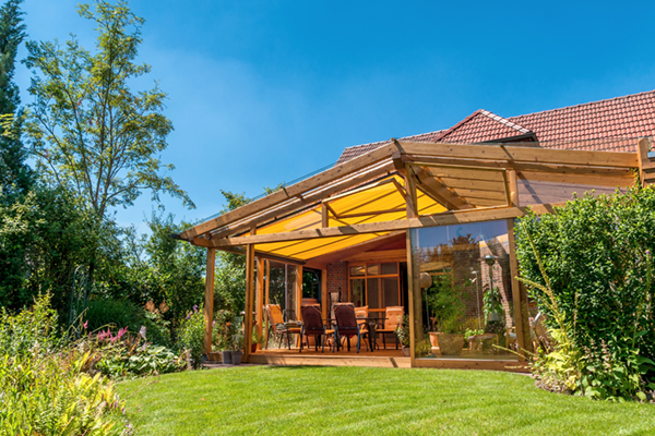 Ein großer, heller Wintergarten oder eine Veranda aus Holz mit Glasdach und Essbereich, umgeben von Garten.