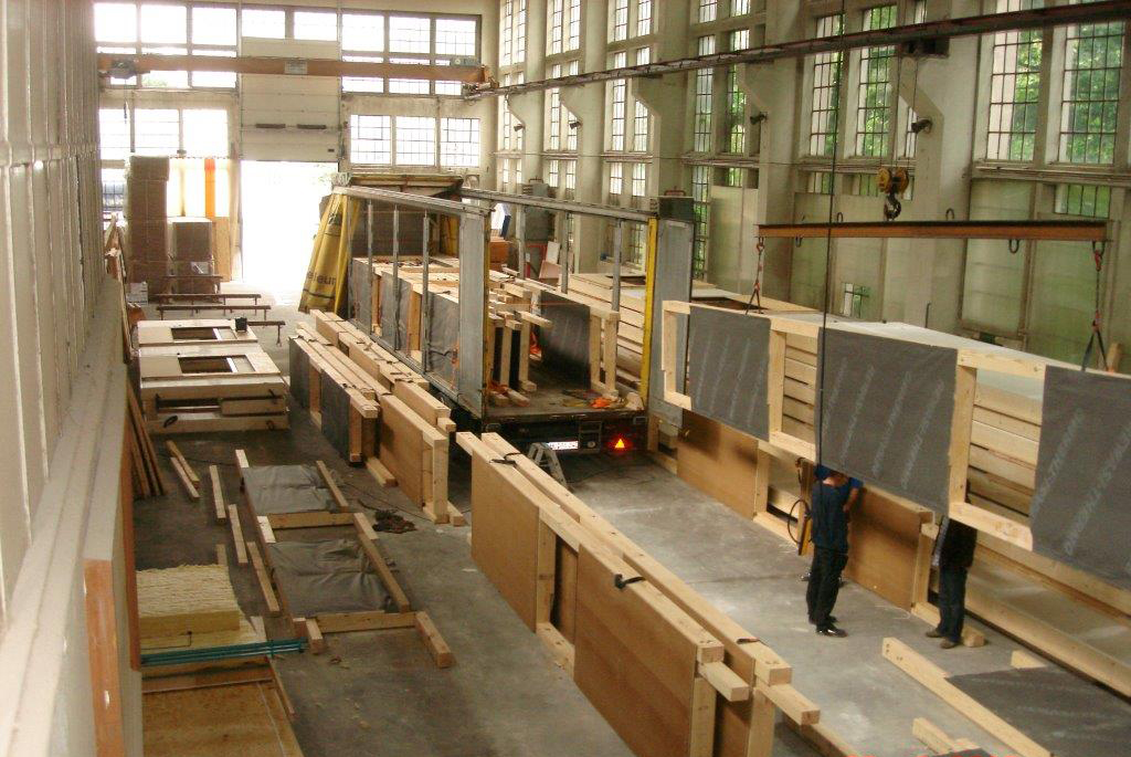 Große Produktionshalle mit vorgefertigten Holzbauelementen, die auf einem LKW verladen werden.