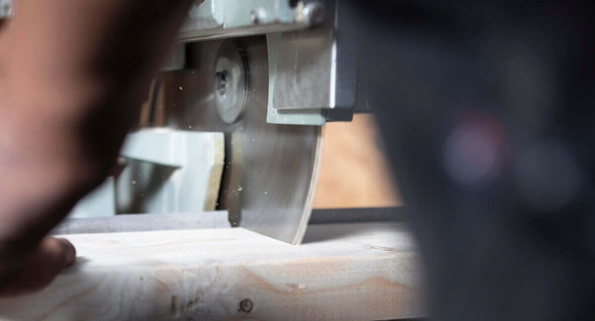 Nahaufnahme einer Kreissäge, die ein helles Holzbrett schneidet, wobei Späne fliegen.