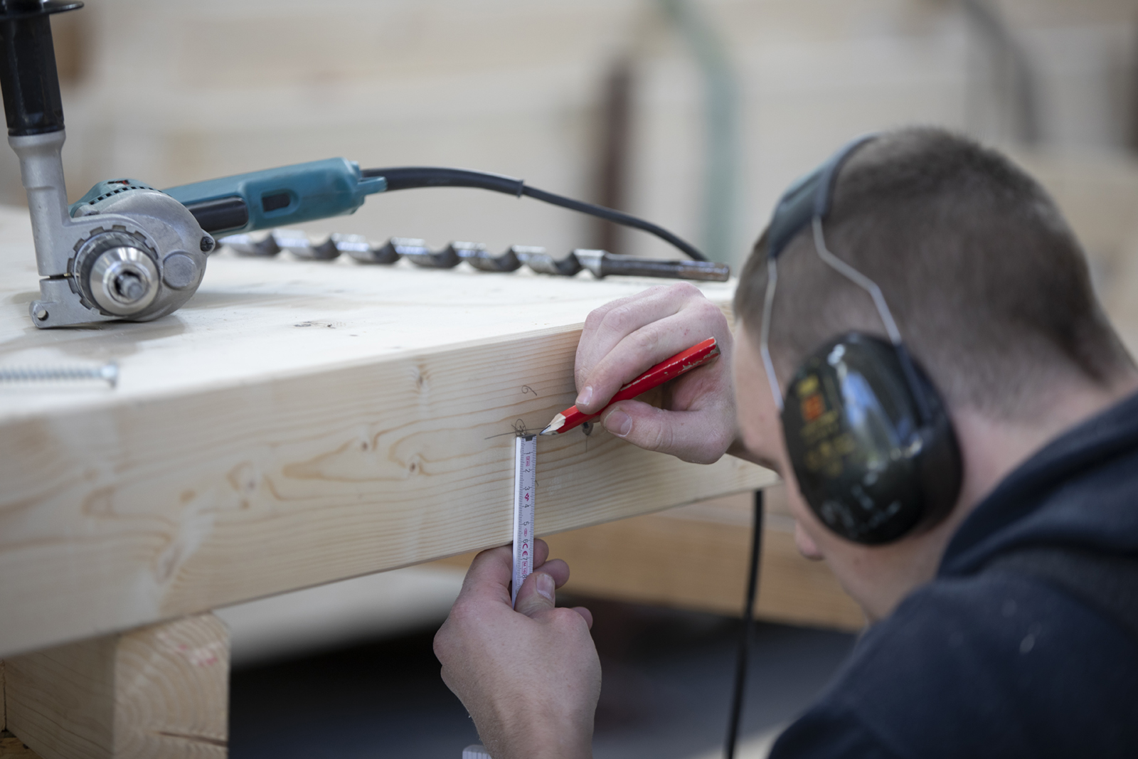 Nahaufnahme von Händen, die mit Maßband und Bleistift ein Holzstück präzise markieren.