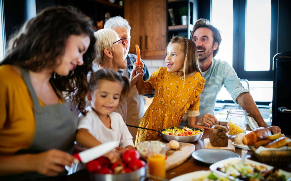 Eine Familie – Eltern, Kinder und Großeltern – kocht gemeinsam in einer Küche, lachend und interaktiv.
