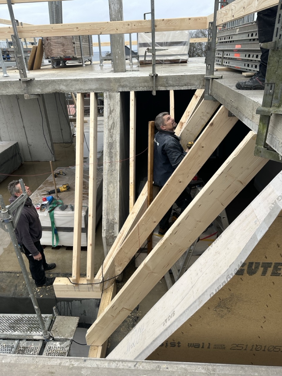 Zwei Handwerker montieren eine Holzkonstruktion im Inneren eines Gebäudes.