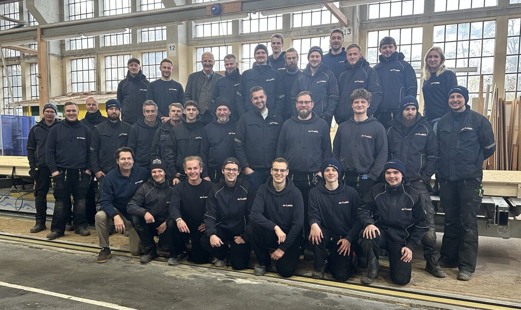 Großes Team der Zimmerei Stamer in einer Werkhalle, gemeinsam für ein Gruppenfoto aufgestellt.