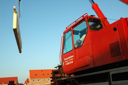 Roter Kran hebt ein vorgefertigtes Bauelement auf einer Baustelle an.